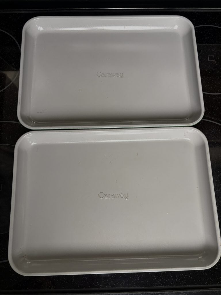 Two Caraway baking sheets on a stovetop with visible marks on their gray baking surfaces