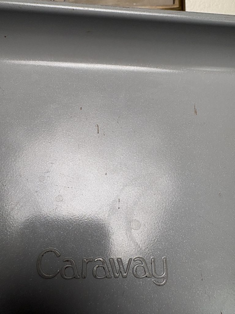 Close-up of scratches and worn green finish near the corner of a Caraway baking sheet’s underside