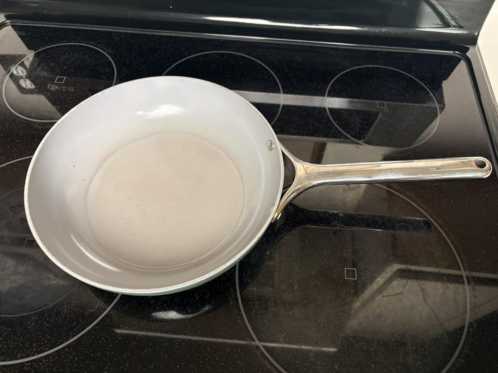 Caraway ceramic frying pan on a glass stovetop, showing small interior scratches and light discoloration after one year of use