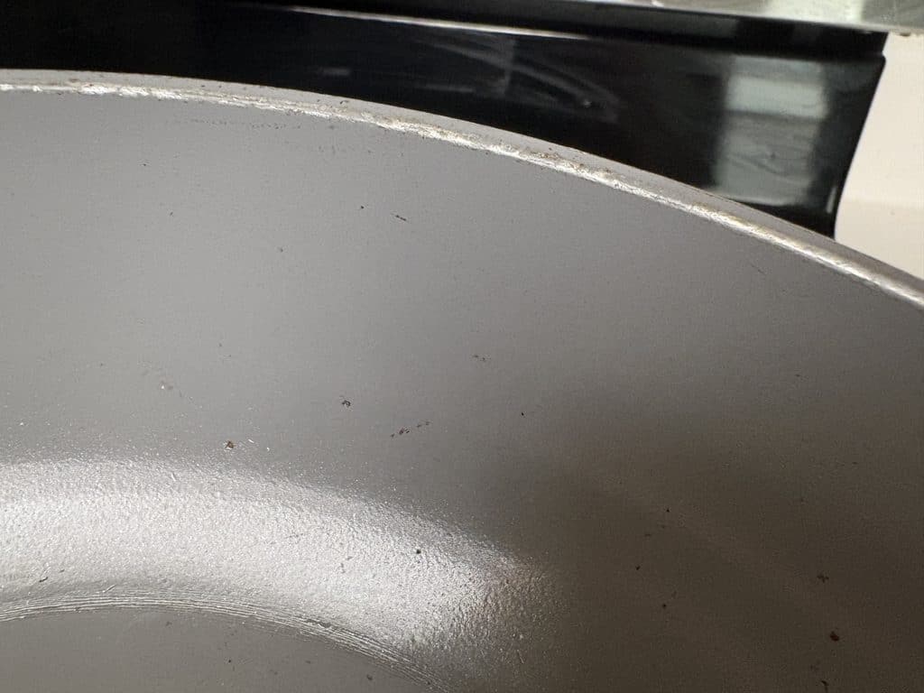 Close-up of a Caraway pan’s inner sidewall, showing scattered dark marks, fine scratches, and a scuffed rim