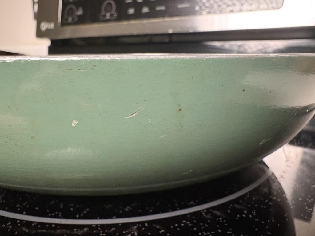 Close-up of the Caraway pan’s exterior, showing small scratches, dark marks, and wear along the rim.