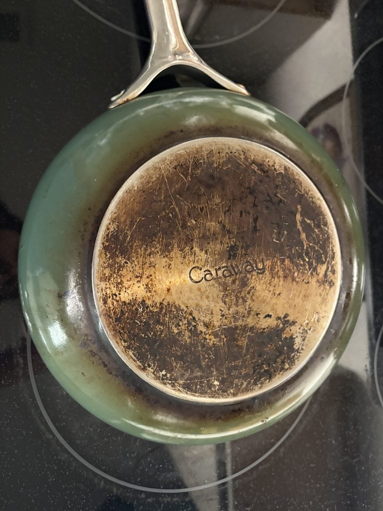 Underside of a sage Caraway frying pan, showing extensive brown discoloration and scratches across the metal base.