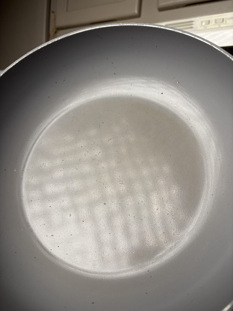 Close-up of a Caraway pan’s gray ceramic-coated interior, showing fine scratches, scattered dark marks, and wear along the rim