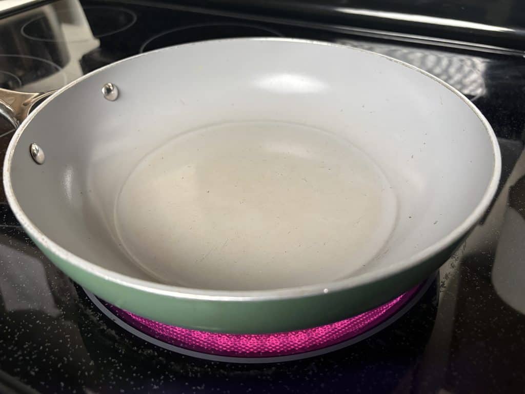Sage Caraway frying pan warming on a glowing electric burner, with light wear visible inside