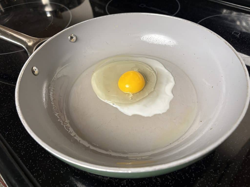 Freshly cracked egg in a Caraway ceramic frying pan, with the white beginning to turn opaque around the edges.
