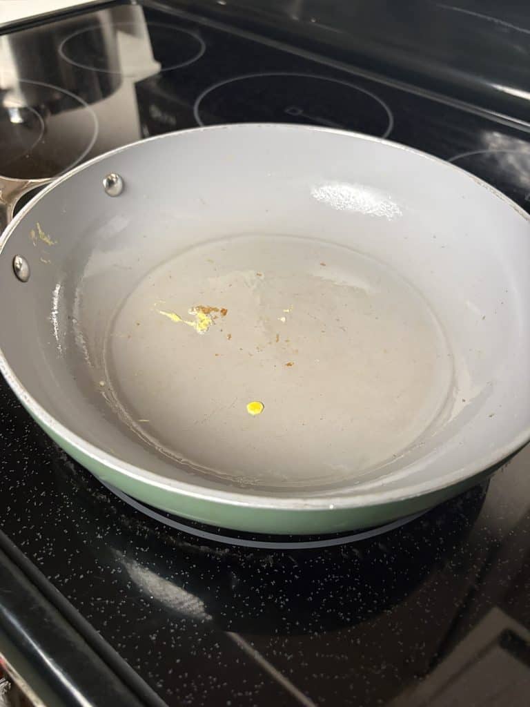 Caraway ceramic pan after cooking an egg, showing a thin layer of oil and small yellow and browned food remnants