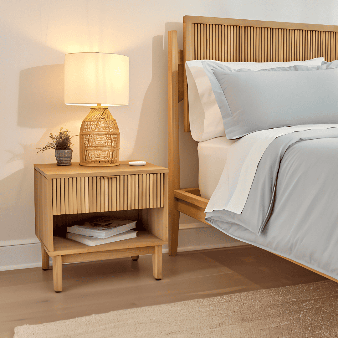 Light wood nightstand with fluted drawer fronts beside a bed.