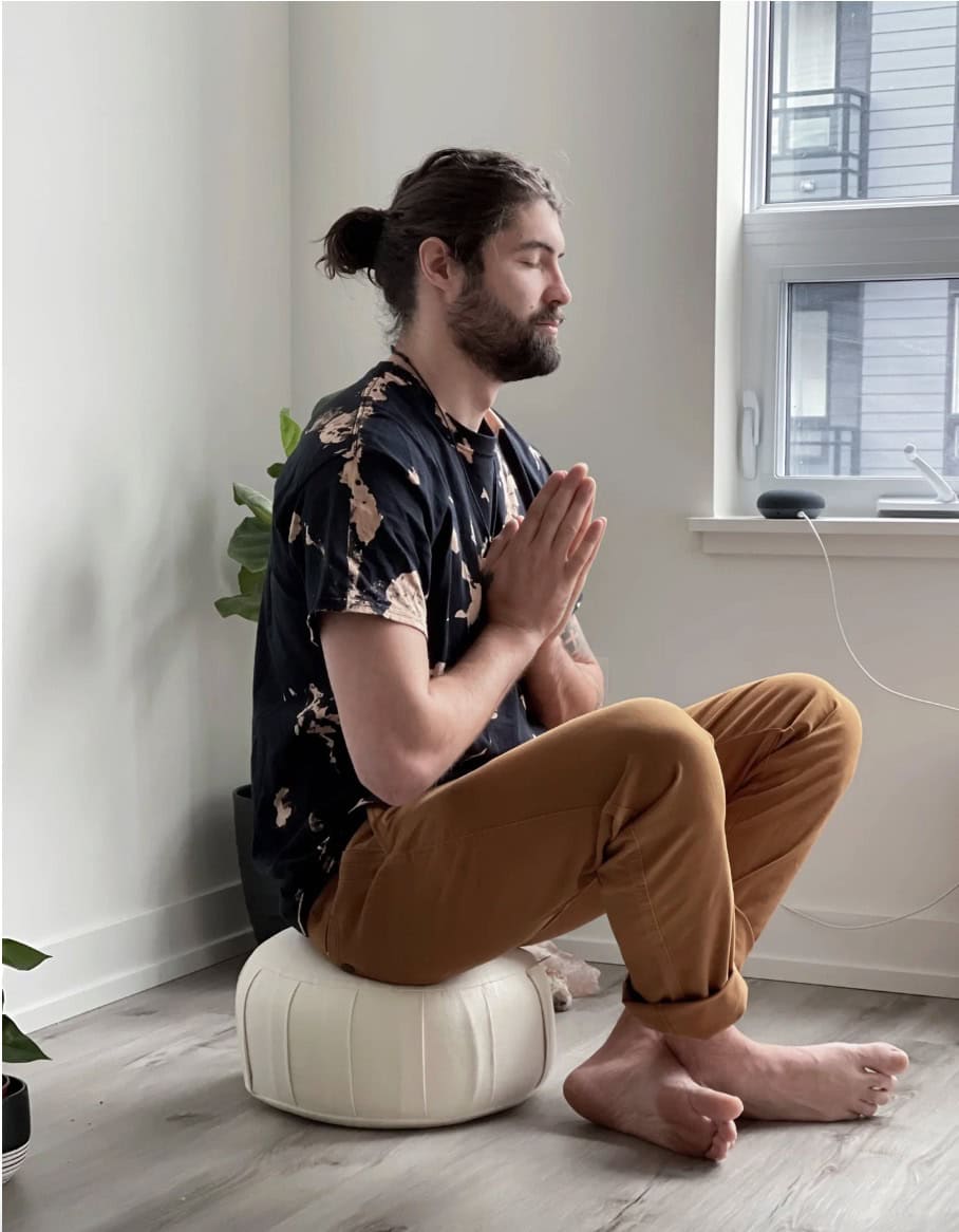 a man sitting on a beige organic cotton meditation cushion