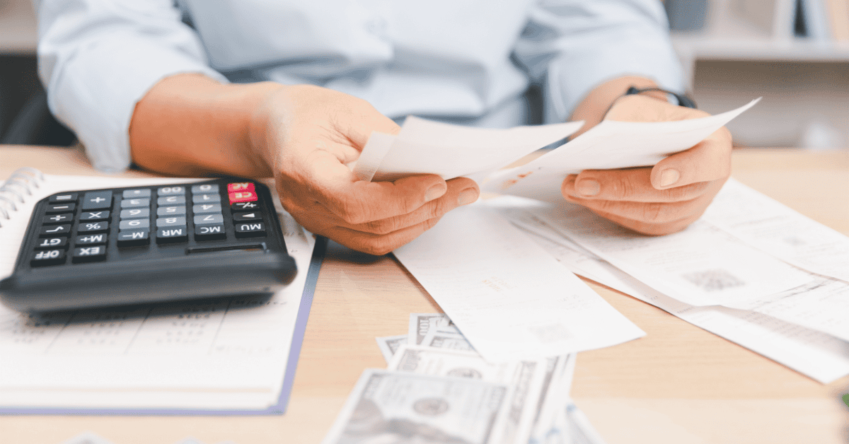 Person reviewing papers beside a calculator and cash on a table