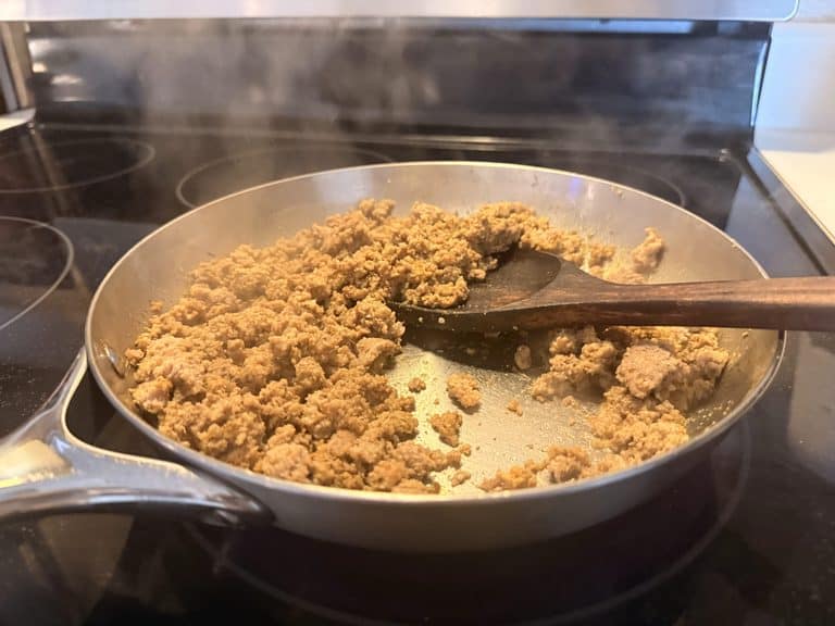 Ground turkey cooking in our Caraway stainless steel pan with a wooden spoon resting inside.