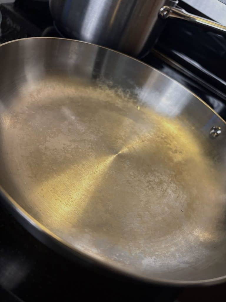 Caraway stainless steel frying pan with cloudy white marks and gold-toned discoloration across the cooking surface