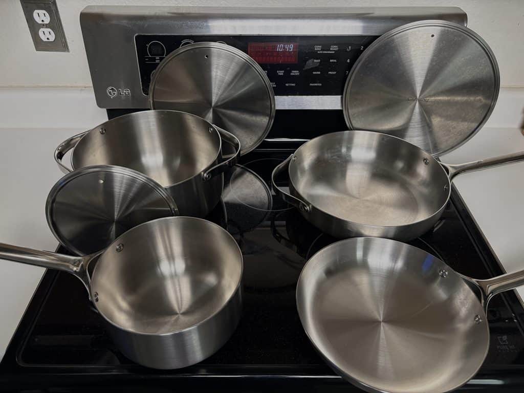 Our Caraway stainless steel cookware set on the stove, with four pots and pans and three lids propped behind them