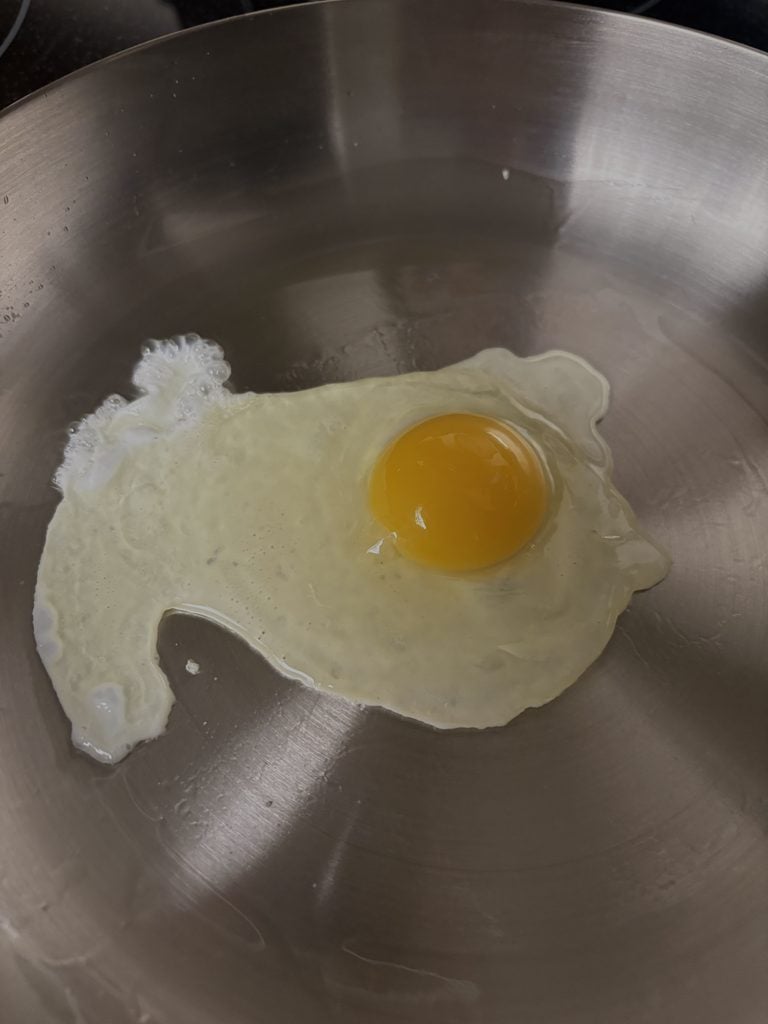 A sunny-side-up egg cooking in olive oil in our Caraway stainless steel frying pan