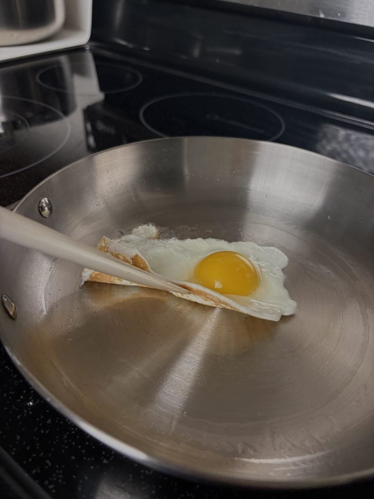 Spatula lifting a fried egg from a Caraway stainless steel pan, revealing its browned underside