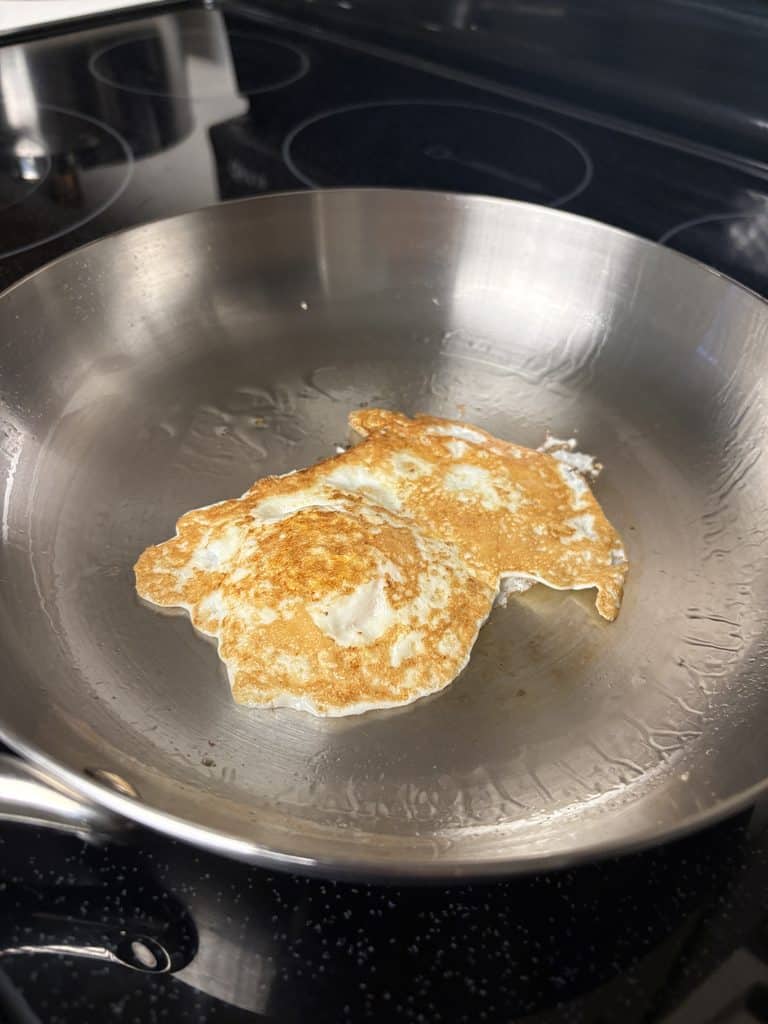 Flipped fried egg with a golden-brown underside in a Caraway stainless steel pan