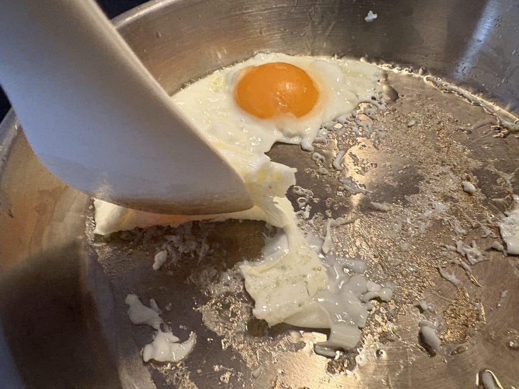 Two fried eggs with torn whites and stuck-on egg residue in our La Sera stainless steel pan