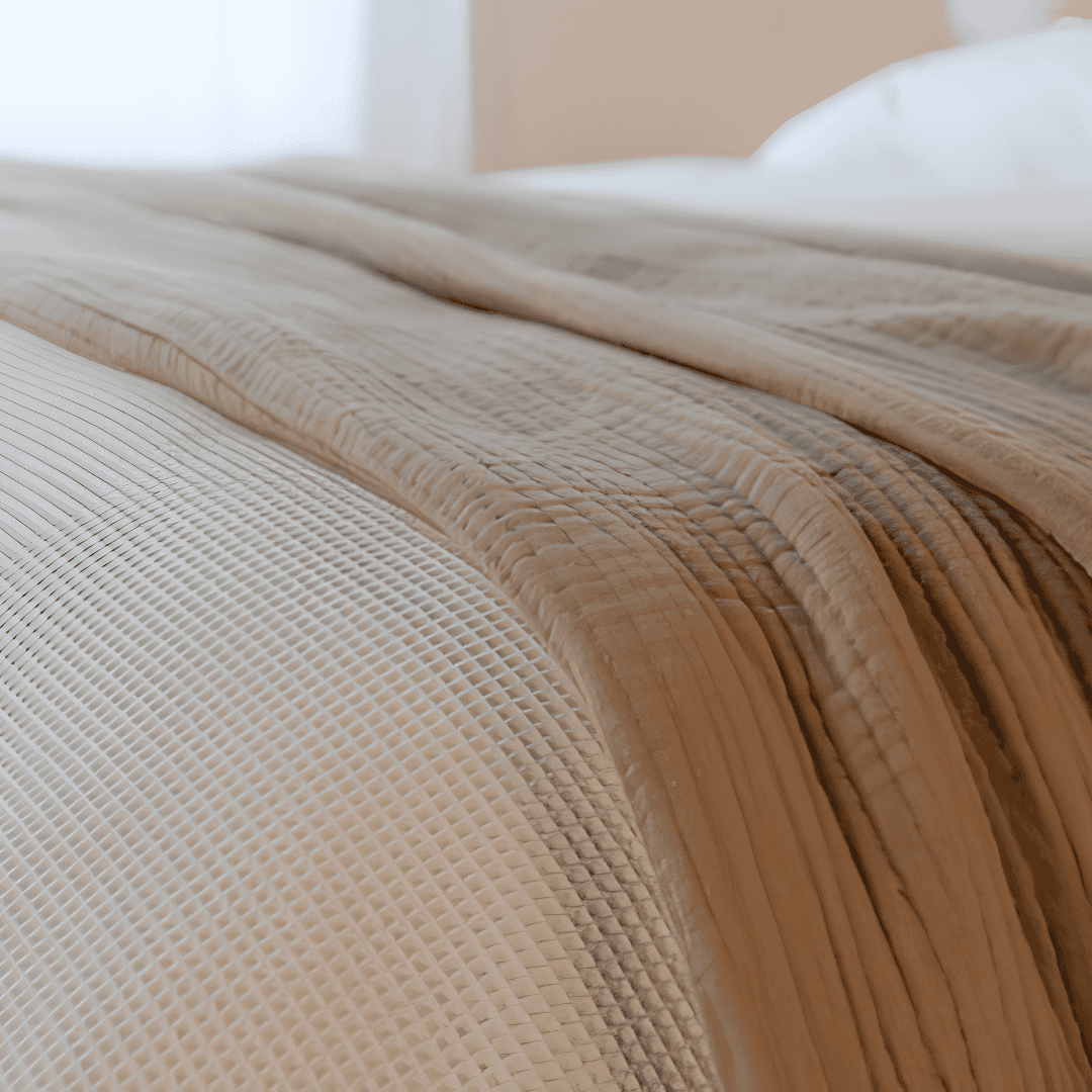 Close-up of layered beige and cream blankets with different woven textures, including an open waffle weave and soft cotton fabric.