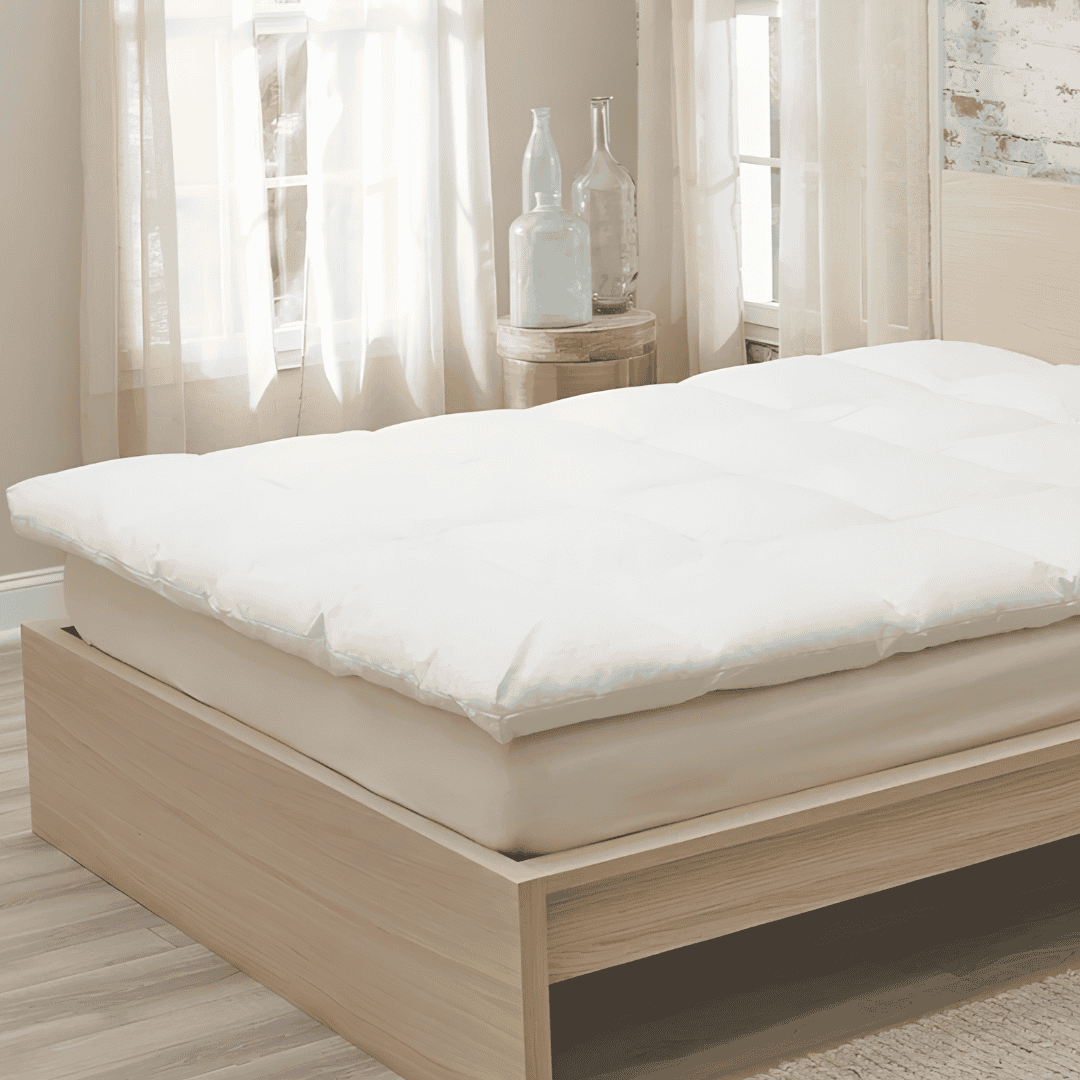 White mattress topper resting on a quilted mattress with a wooden headboard, bedside table, and natural sunlight.