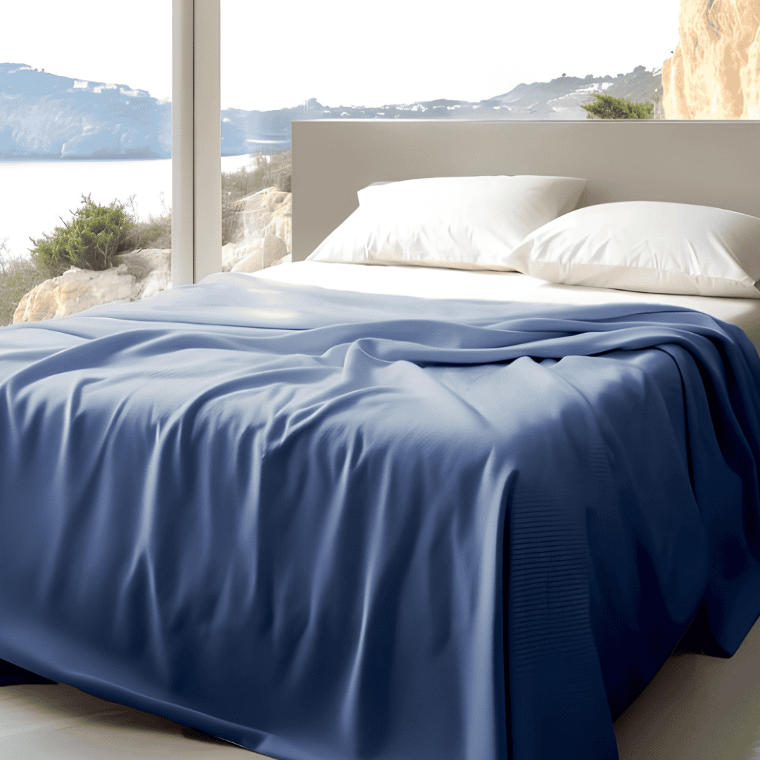 Light-filled bedroom with a smooth blue blanket draped across a bed with white pillows and a scenic mountain and water view.